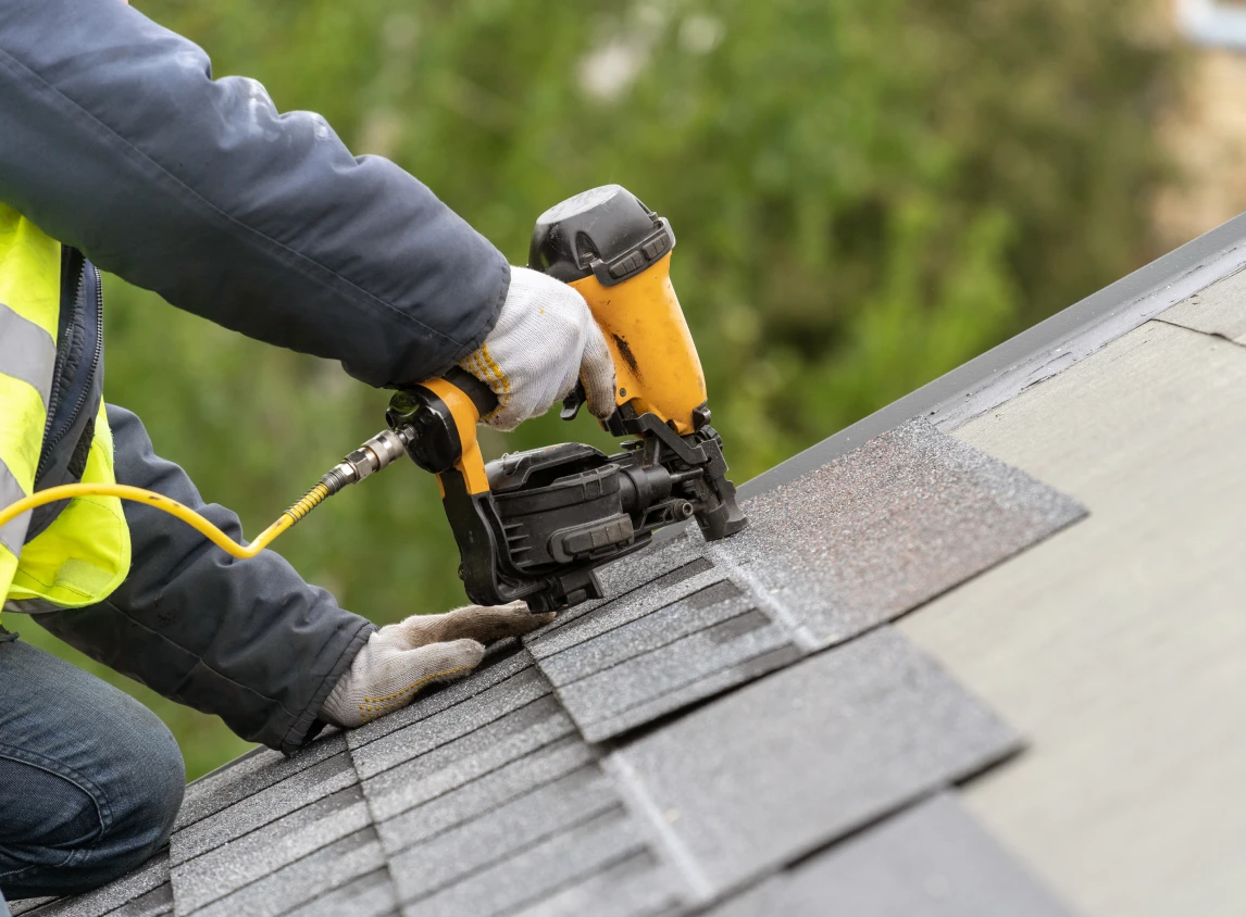Worker using nail gun on roof shingles